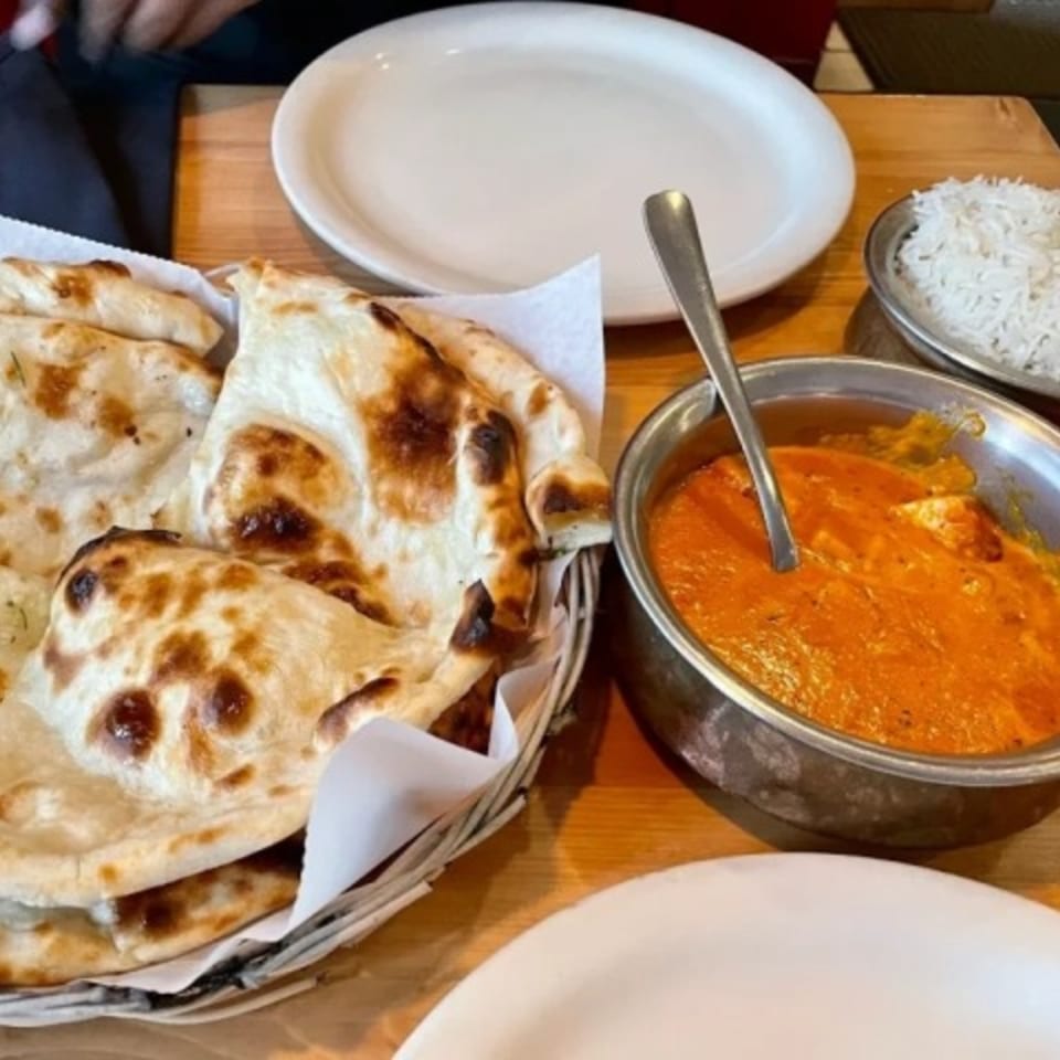 Indian butter chicken or paneer, naan bread, and rice on a wooden table at Bombay South.