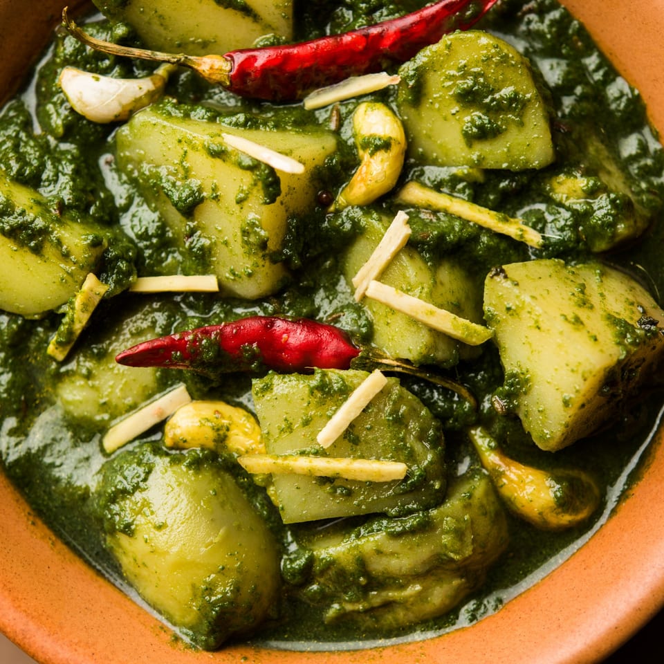 Close-up of Bombay South's Aloo Palak, featuring potatoes in vibrant green spinach gravy with red chilies and ginger.