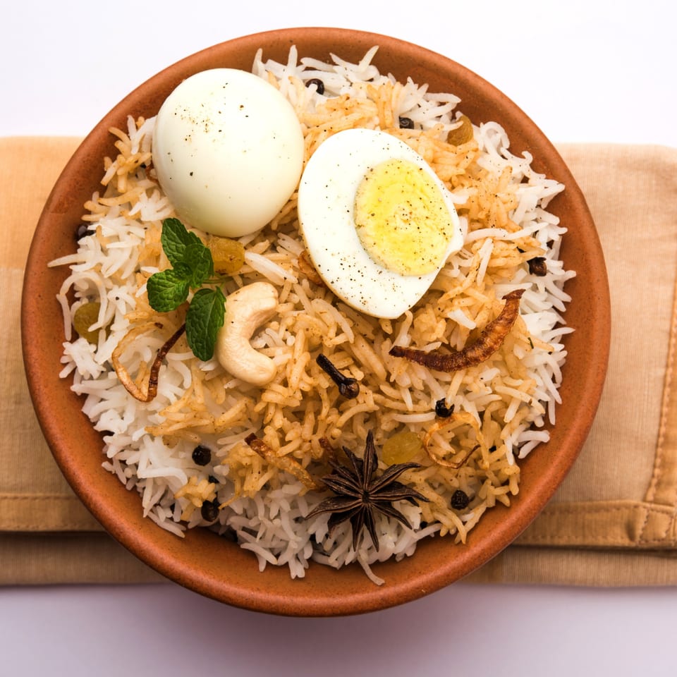 Egg biryani in a terracotta bowl, garnished with mint, cashews, and spices.
