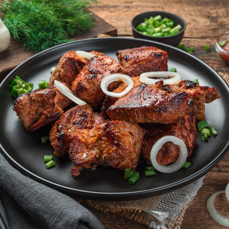 Grilled Indian meat skewers with onion rings and green onions on a black plate.