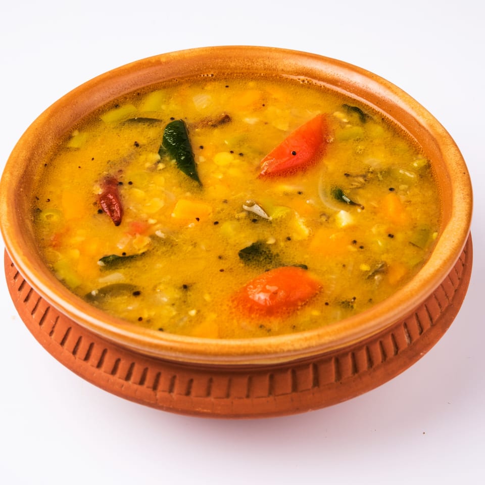 A close-up of Bombay South's Indian sambar, a yellow lentil and vegetable stew, in a terracotta bowl.